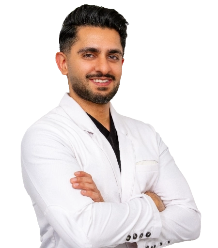 DrMehta_half_optimized Dr. Joshua Kindelan is captured in a professional portrait wearing a white lab coat over a blue plaid dress shirt and a yellow tie. He is standing with his arms crossed in a clinical environment.